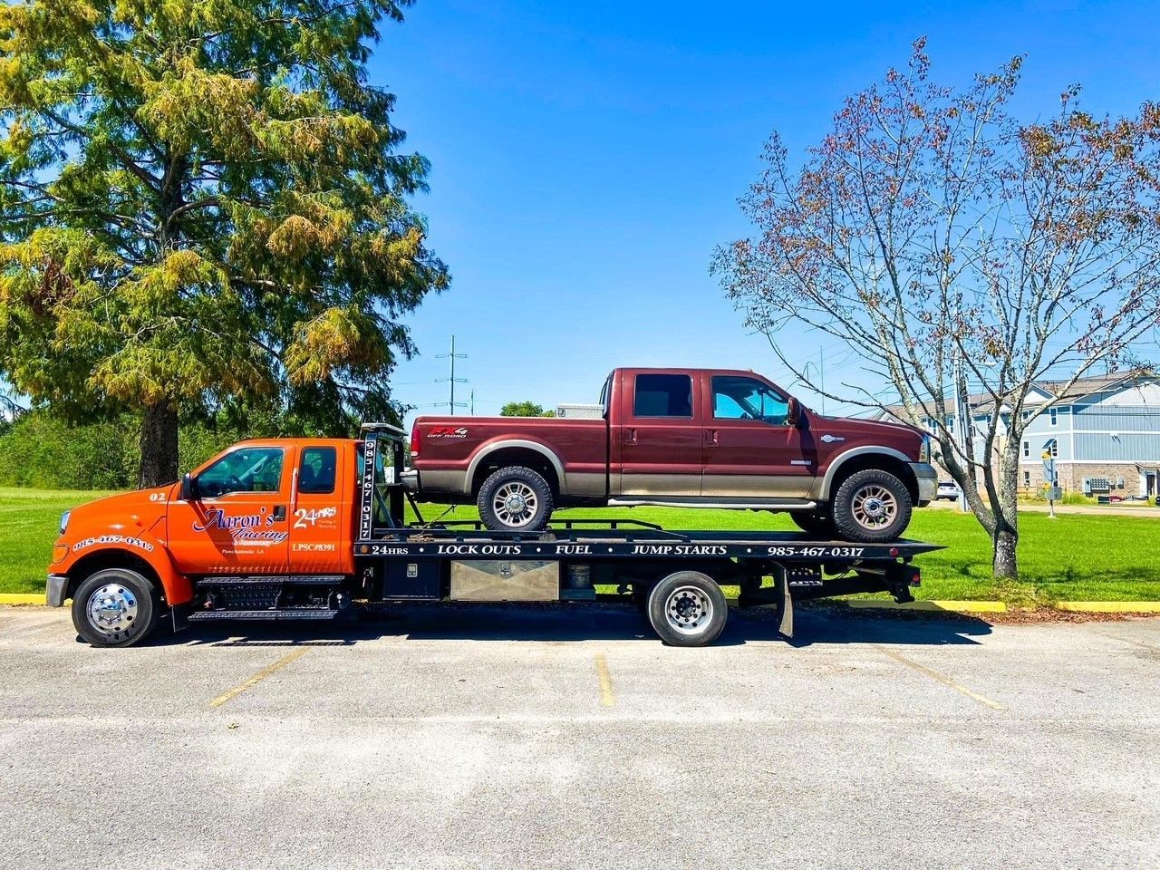 A picture of a tow truck with a maroon truck on the back of it with trees in the background in Madisonville, LA